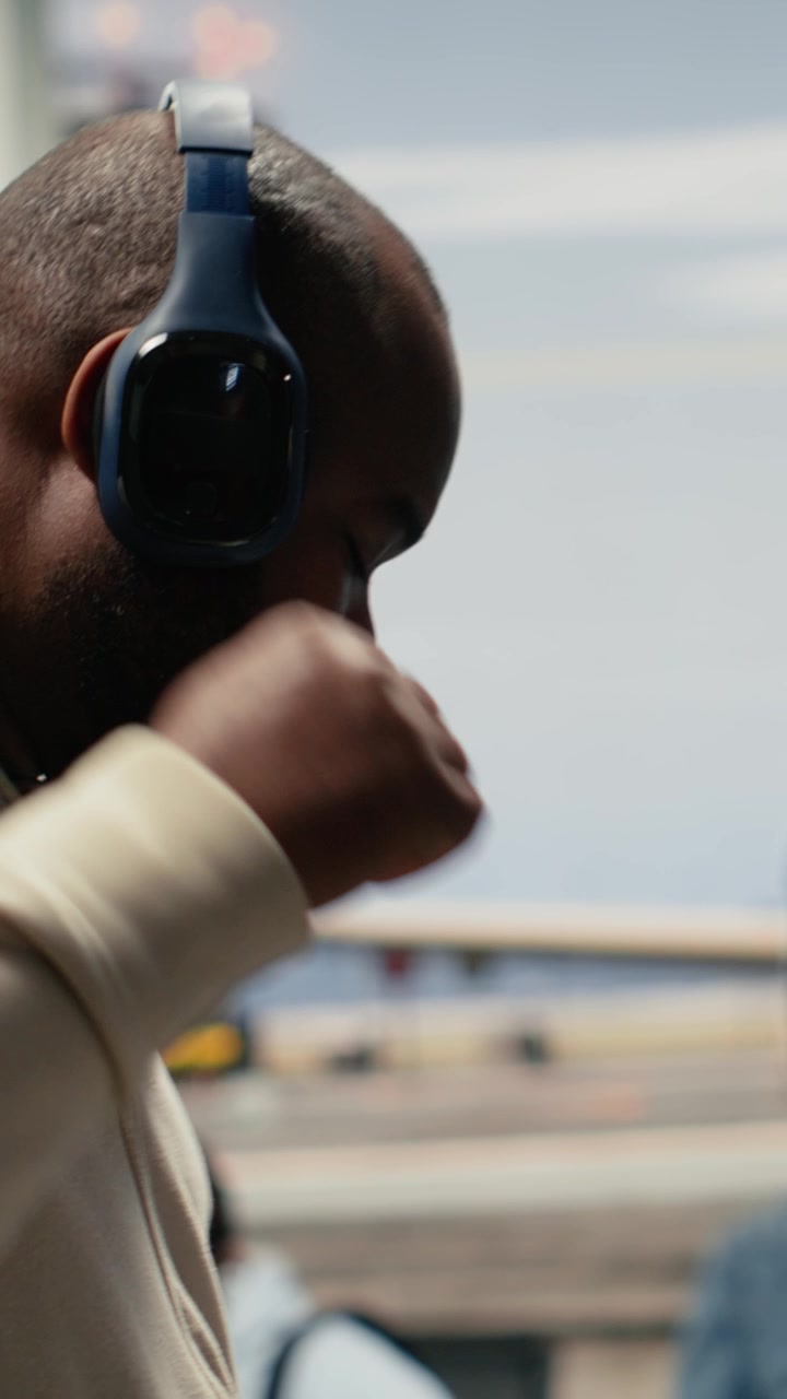 Video verticale: Uomo che si muove in un corridoio affollato dell'aeroporto con le cuffie audio.