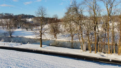 aerial snow falling over river waterway with leafless trees and white banks