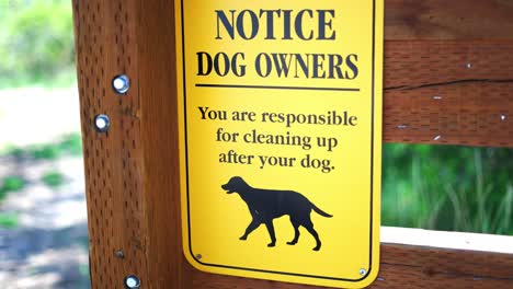 notice to dog owners you are responsible for cleaning up after your pet bright yellow sign at public park hiking trail, panning back and forth keeping sign in frame, in 4k slow motion