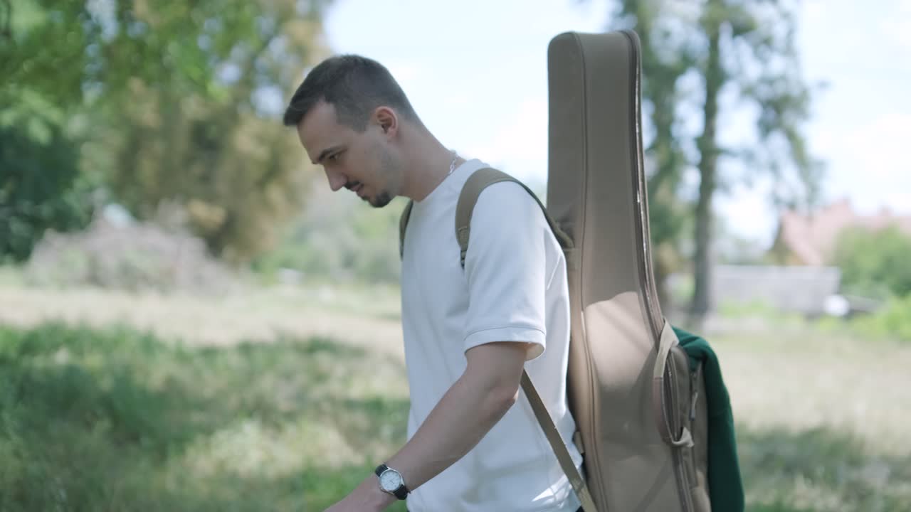 숲 근처의 거리에서 기타를 들고 는 젊은 남자