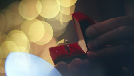 groom hands opening ring red box at evening lights blurred background closeup