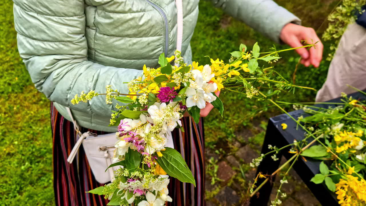 Kvinde i traditionel stribet nederdel laver blomsterkrans under lettisk midsommerfest