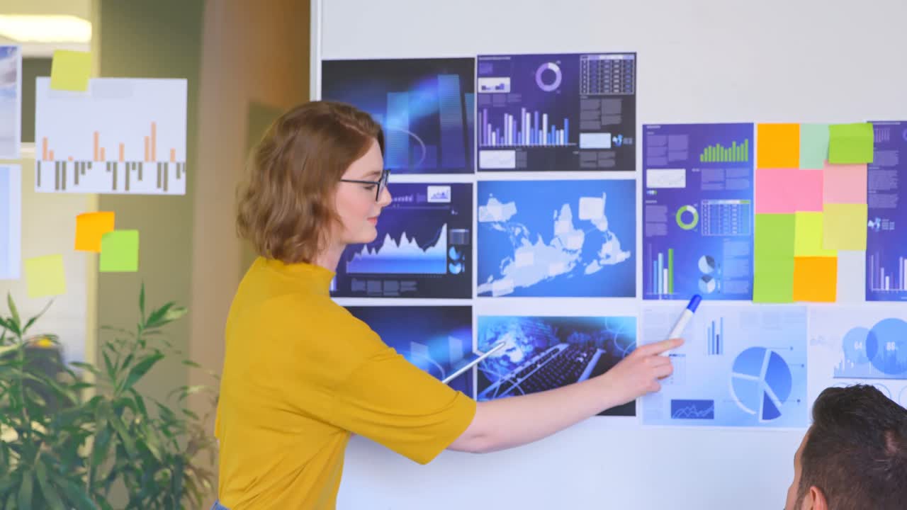vista lateral de una joven ejecutiva caucásica explicando el gráfico a un compañero de trabajo en una oficina moderna 4k