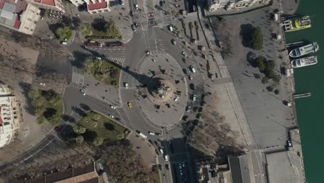 aerial: overhead shot of columbus monument roundabout in barcelona, spain with busy car traffic on sunny day [4k]