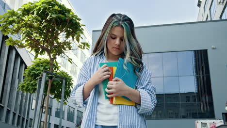 una adolescente con libros afuera de un edificio escolar