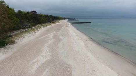 Aerial-Shot-of-Ystad-Saltsjöbad-in-South-Sweden-Skåne-Near-The-Ocean-Östersjön-With-People-Running-By-The-Beach-In-a-Cloudy-Day