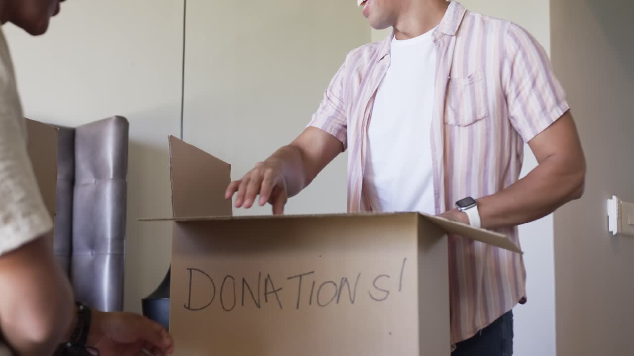 African American men packing into DONATIONS! box deciding to donate, folding pink sweater in room