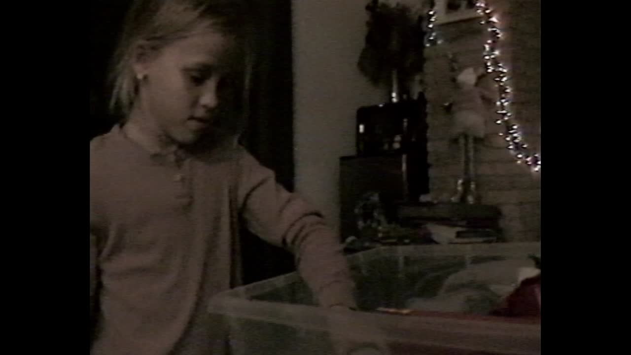 Girl examining toy near Christmas tree in VHS footage