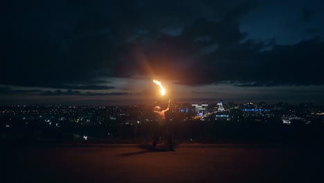 Young-blond-male-does-tricks-with-fire-breaths-fire-at-night-with-city-skyline-in-the-background