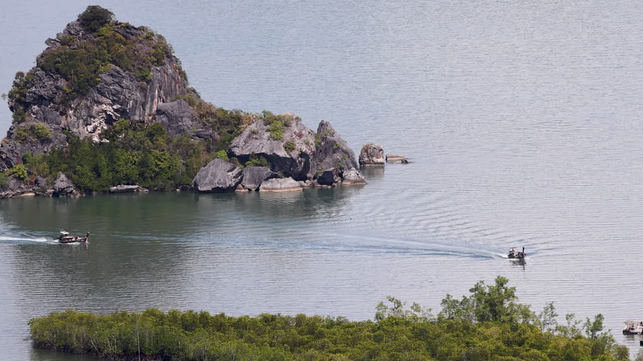 Small boats glide through calm waters near a rocky island in Phang Nga, Thailand. The tranquil scene captures natural beauty and motion