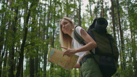 young woman traveler with map and backpack relaxing outdoor at nature trail on summer vacations day. lifestyle hiking concept. wood trip. picking direction with a map.