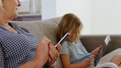 grandmother and granddaughter using mobile phone and digital tablet in living room 4k