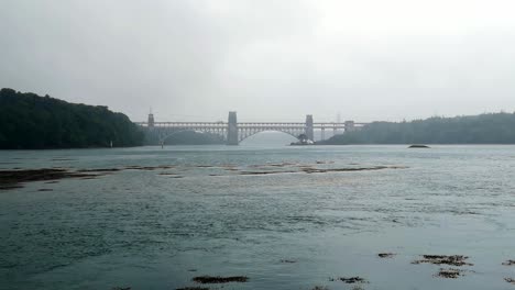 Blue-coloured-misty-overcast-Menai-Straits-Britannia-bridge-crossing-into-Anglesey,-Wales