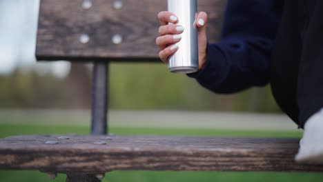 Una-Mujer-Recoge-Una-Lata-De-Bebida-De-Aluminio-Brillante-De-Un-Banco-De-Madera-Al-Aire-Libre