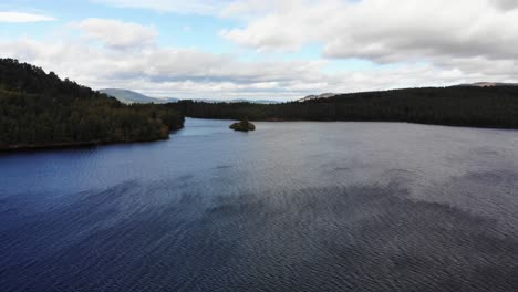 Vuelo-Aéreo-Sobre-La-Superficie-Del-Lago-An-Eilein-Rodeado-De-Pinos-Del-Bosque-De-Rothiemurchus