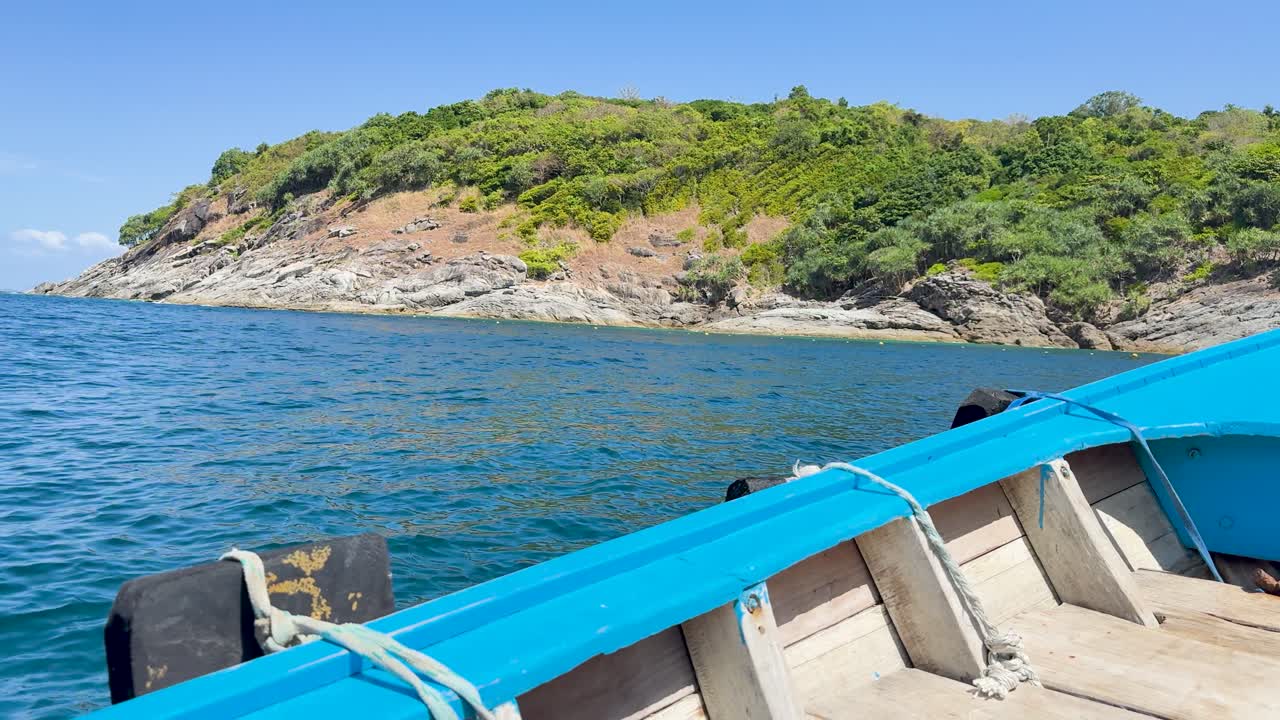 A boat glides past lush, rocky shores under clear skies in Phuket, Thailand, capturing serene coastal beauty