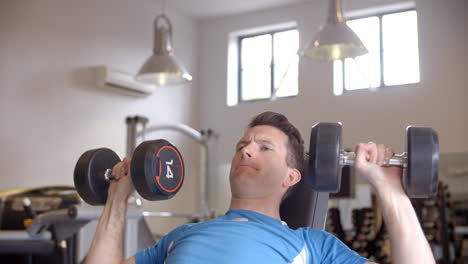 man works out with dumbbells on a bench at a gym, front view