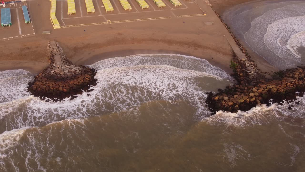 vista aérea de arriba hacia abajo del rompeolas en la costa, poderosas olas de agua del océano alcanzando la playa de arena de mar del plata durante la puesta de sol, argentina