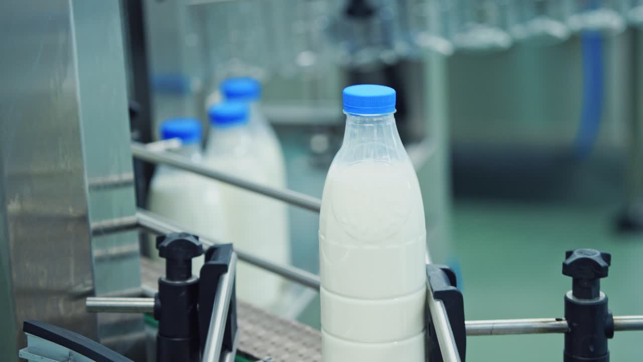Milk bottles on conveyor belt. Slow motion of bottles with fresh milk. Beverage production line at dairy factory. Modernized milk bottling plant. Close-up.