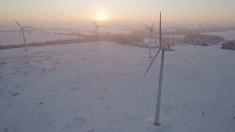 A-rotating-windmill-as-an-energy-generator-is-located-in-Northern-Germany-near-the-A1-motorway,-sunset-snowy-landscape