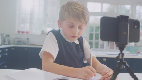 Niño-En-Casa-Usando-Uniforme-Escolar-Teniendo-Una-Lección-En-Línea-A-Través-De-Videollamada-En-Un-Teléfono-Móvil