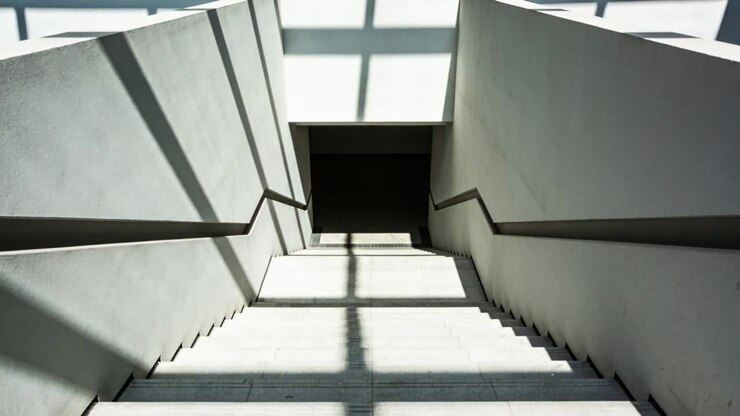 Shifting sunlight casting grid shadows across concrete staircase at stairwell to dark opening