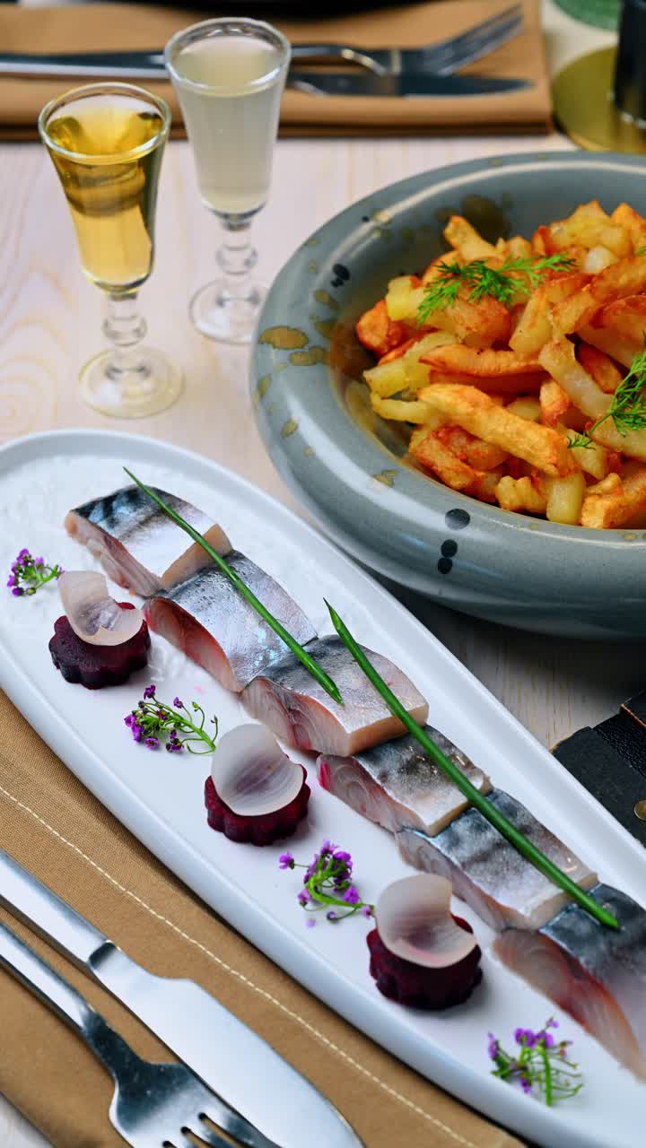 Aringa salata affettata con barbabietola e patate fritte. Filetto di aringa affettato su un piatto bianco con barbabietola, cipolle e una ciotola di patate fritte dorate.