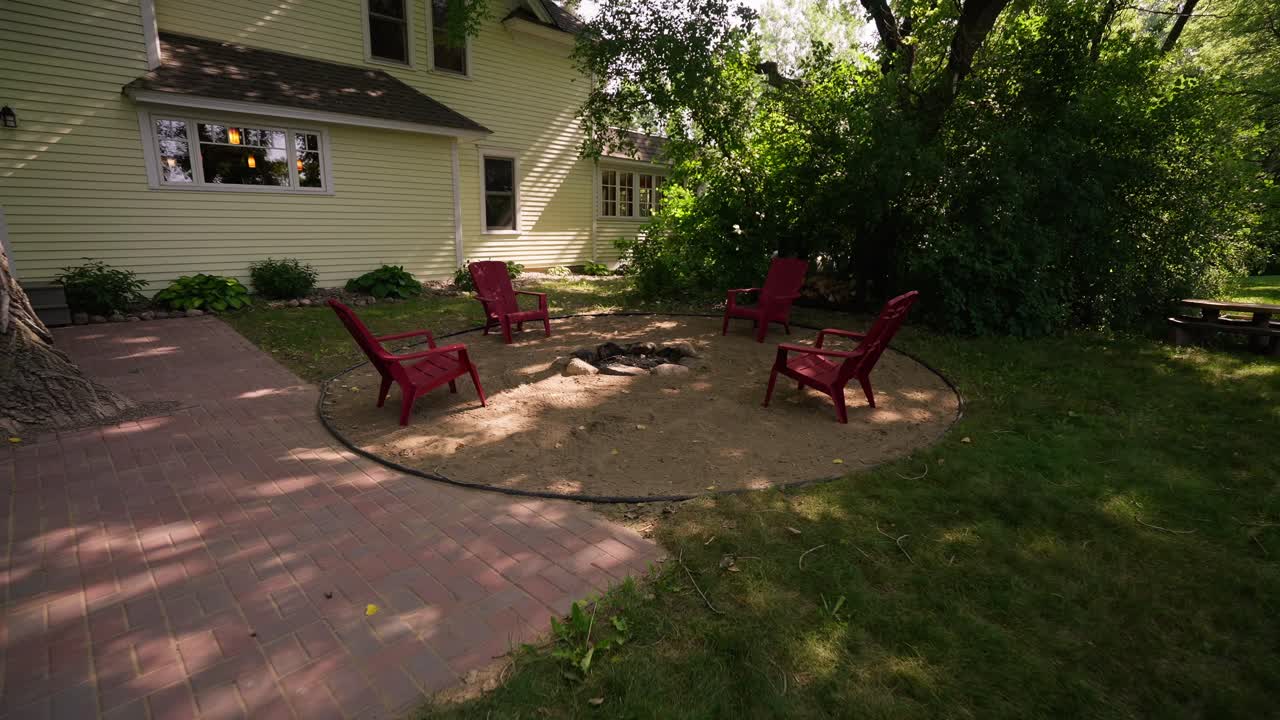 wide pull back of a fire pit surrounded by sand and red Adirondack chairs