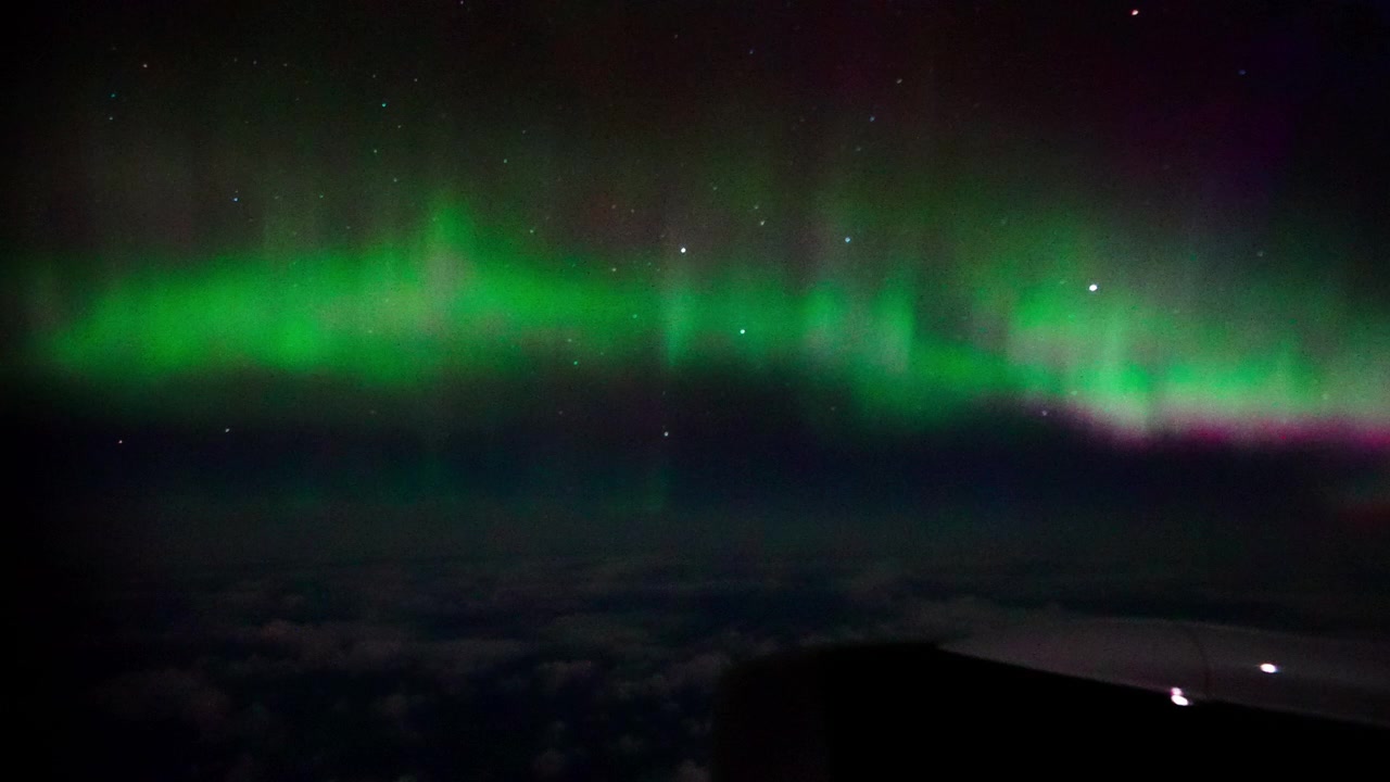Splendida aurora boreale verde e viola che luccica sopra nuvole scure e stelle, catturata da un aereo ad alta quota. Autentico fenomeno del cielo notturno per progetti di viaggio e scientifici.