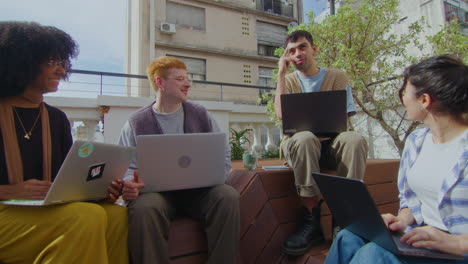 gen z people working with laptops and having talk outdoor in the city