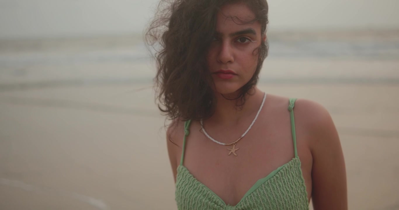 La telecamera si allontana lentamente da una giovane donna in posa sulla spiaggia