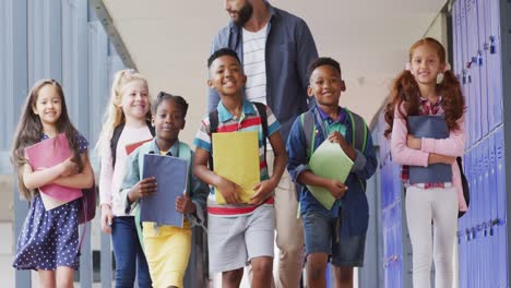 Diverse-male-teacher-and-happy-schoolchildren-walking-at-school