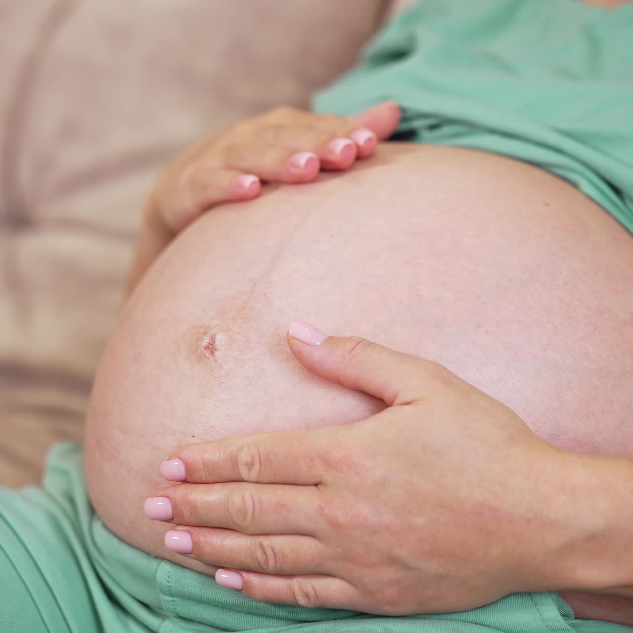 Pancia scoperta di una donna incinta. Donna incinta che accarezza il suo ventre mentre è sdraiata su un divano a casa. Primo piano. Concetto di gravidanza