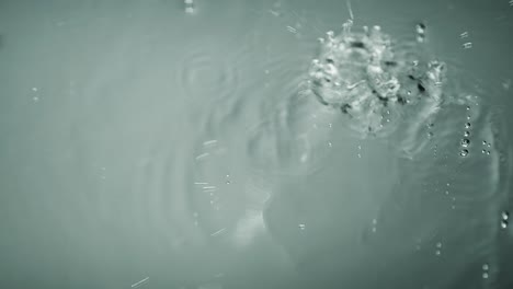 water drops fall on a plain white mirrored surface. they splash in slow motion in close up.