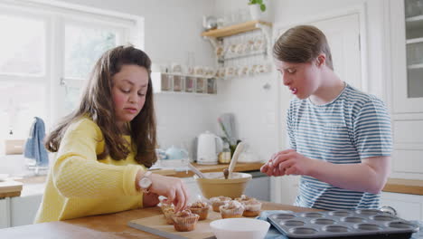 young downs syndrome couple decorating homemade cupcakes and dancing in kitchen at home