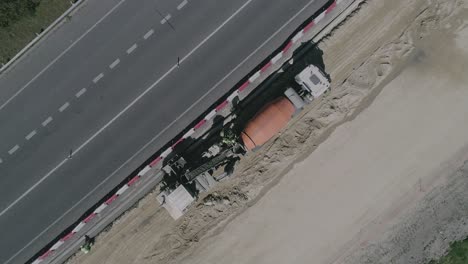 Toma-Aérea-De-Arriba-Hacia-Abajo-De-Un-Equipo-De-Contratistas-De-La-Construcción-Trabajando-Duro-Al-Lado-De-Una-Concurrida-Carretera-Urbana-Un-Gran-Camión-Mezclador-De-Hormigón-Descargando-Material-Fresco-Para-Que-Los-Trabajadores-Preparen-Galicia-España