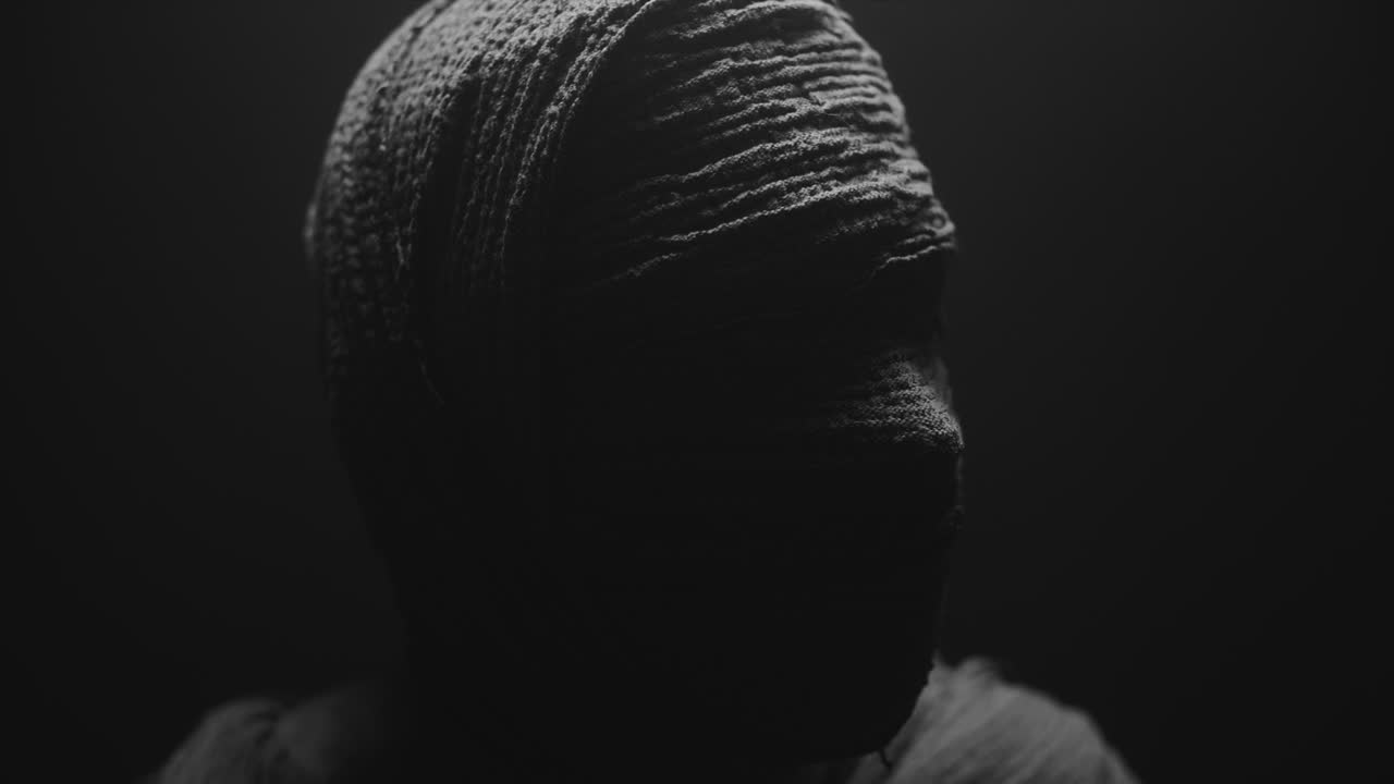 A mummy of a woman on a dark backdrop rises  and then turns her head