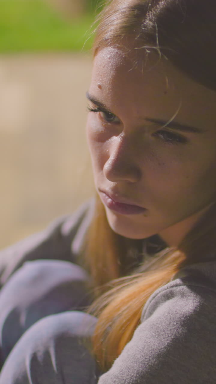 primer plano de una joven cansada sentada en un banco al aire libre por la noche, pareciendo somnolienta y contemplativa, rodeada de un fondo suave y borroso