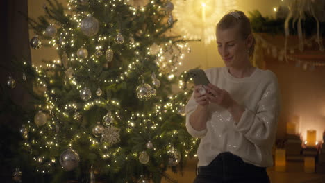 una mujer tomando una selfie junto a un árbol de navidad.