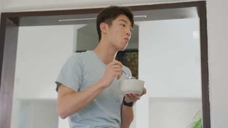 asian male teenager looking away and having breakfast in living room