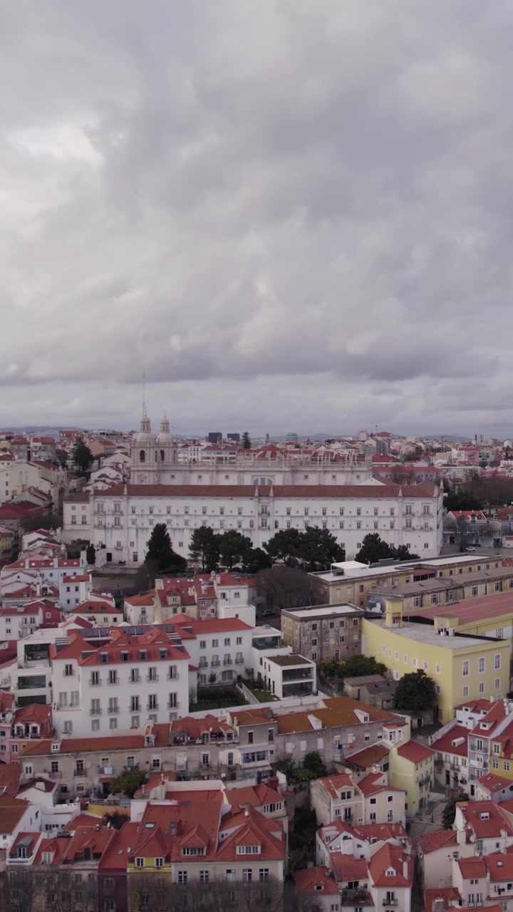 Scenic vertical drone orbit over the National Pantheon and São Vicente de Fora, with historic rooftops and Lisbon cityscape below.