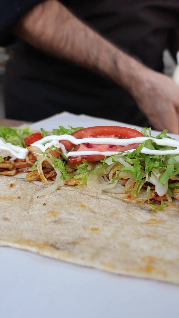 Chef che aggiunge salsa bianca a un involtino di kebab fresco.