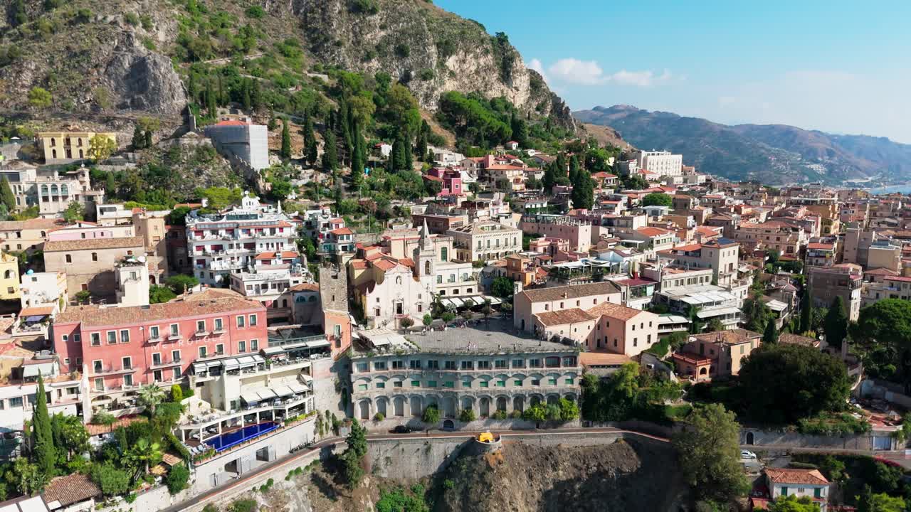 Aerial pull-away shot starting at Piazza IX Aprile, gradually revealing the historic town of Taormina and its scenic hillside setting