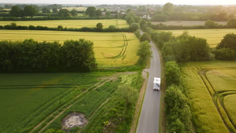 aerial view tracking a rv driving in middle of blooming rapeseed fields, sunset