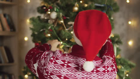 back view of man wearing santa hat and decorating christmas tree at home