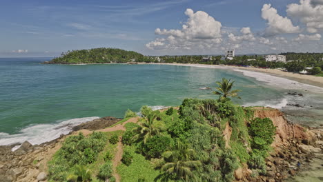 Mirissa-Sri-Lanka-Aerial-v17-drone-flyover-bay-across-Parrot-rock-capturing-golden-sandy-beach-and-hillside-tropical-landscape-views-on-a-sunny-day---Shot-with-Mavic-3-Cine---April-2023