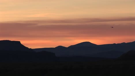 Long-shot-of-a-helicopter-flying-over-low-hills-at-goldenhour