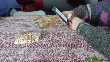 mujer blanca comiendo maní en una mesa y usando un teléfono celular