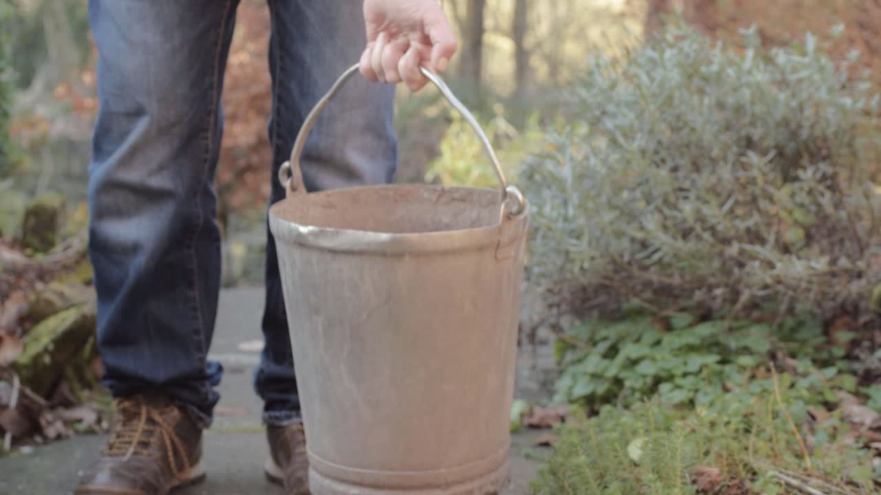 Lady carrying putting metal bucket on garden pathway