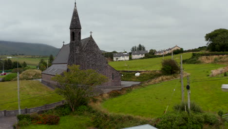 Fly-over-road-in-village-and-heading-to-old-stone-church-with-tower.-Beautiful-medieval-landmark.-Ireland